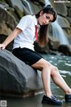 A woman sitting on a rock in front of a waterfall.