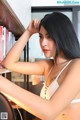 A woman in a white bra top leaning against a bookshelf.