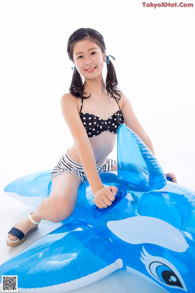 A young girl in a bikini sitting on an inflatable shark.