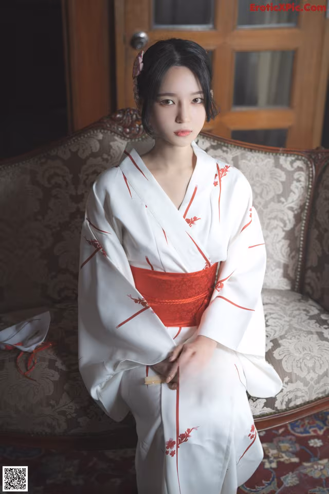A woman in a white and red kimono sitting on a couch.