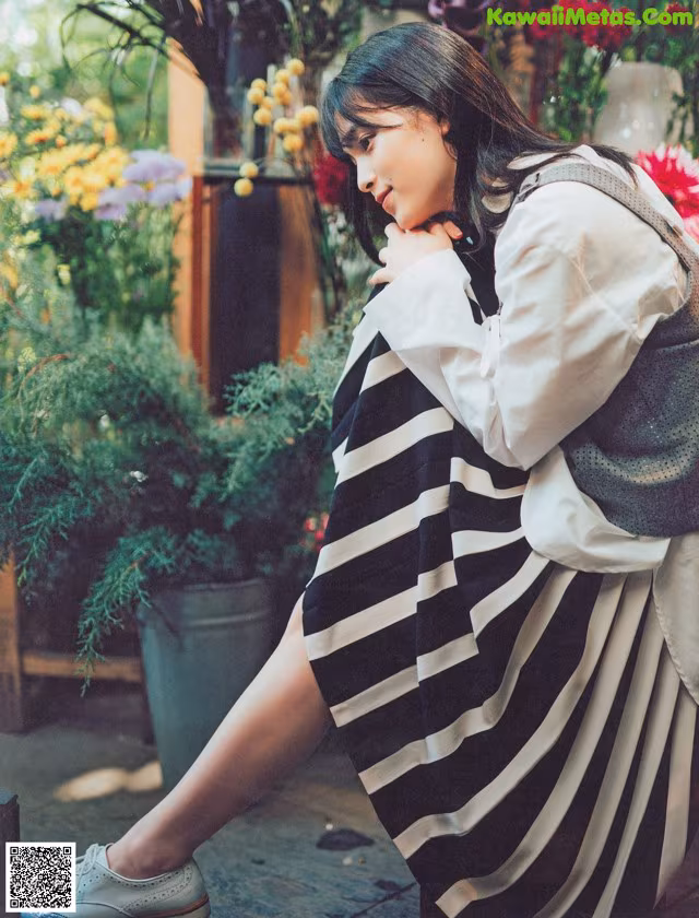 A woman in a black and white striped dress sitting on a bench.