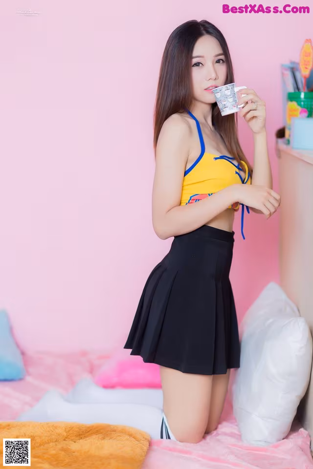 A woman in a yellow top and black skirt holding a cup of coffee.
