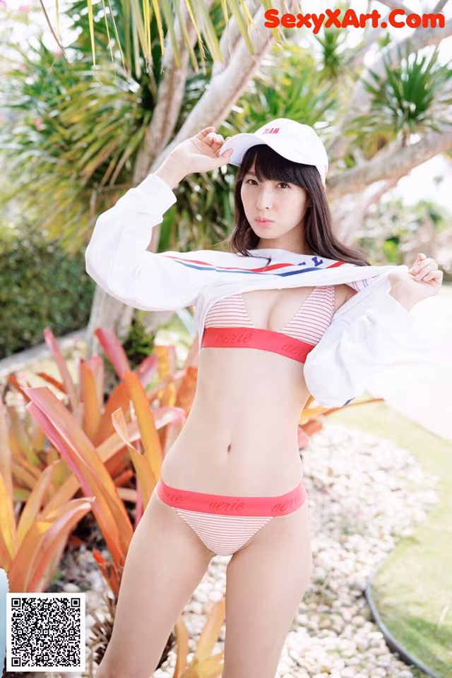 A woman in a bikini and a baseball cap posing for a picture.