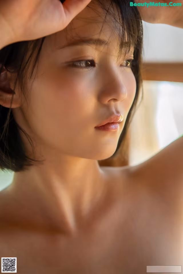 A naked asian woman with her hands on her head.