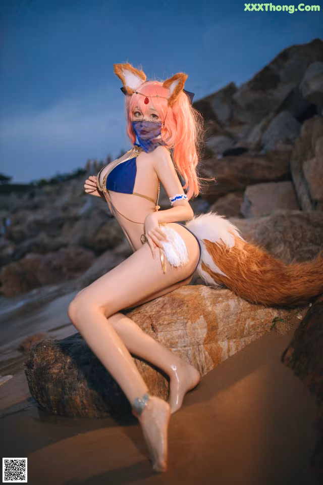 A woman in a bikini sitting on a rock on the beach.